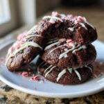 A stack of fudgy double chocolate peppermint cookies drizzled with white chocolate and topped with crushed candy canes.