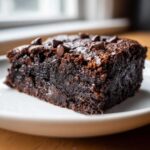 A close-up of a fudgy slice of sweet potato brownies topped with chocolate chips on a white plate.