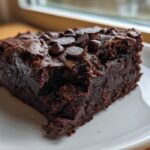 A close-up of a fudgy slice of sweet potato brownies topped with melted chocolate chips on a white plate.