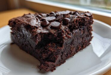 A close-up of a fudgy slice of sweet potato brownies topped with melted chocolate chips on a white plate.