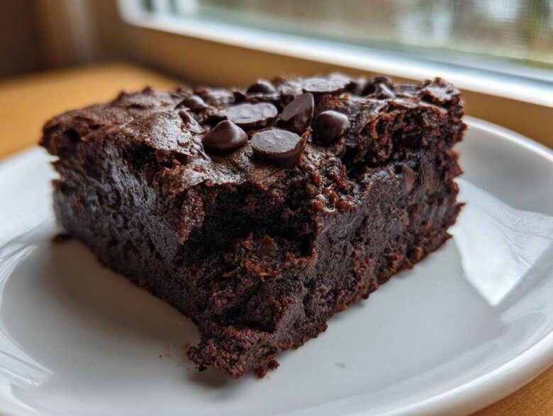 A close-up of a fudgy slice of sweet potato brownies topped with melted chocolate chips on a white plate.