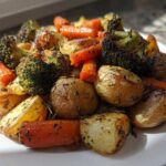 A close-up of perfectly caramelized Garlic Herb Roasted Veggies including potatoes, carrots, and charred broccoli.