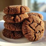 A stack of dark, crinkled gingersnap cookies coated heavily in sparkling sugar crystals on a white plate.