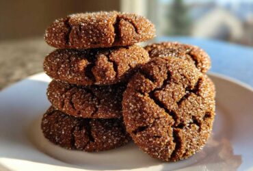 A stack of dark, crinkled gingersnap cookies coated heavily in sparkling sugar crystals on a white plate.