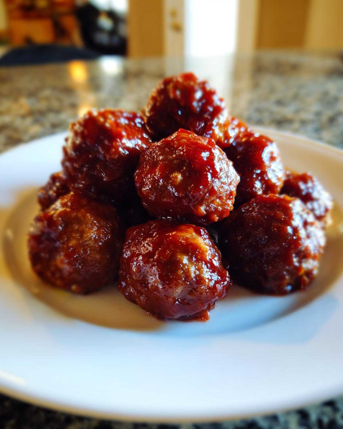 A close-up of several glossy, sauce-covered cranberry meatballs piled high on a white serving plate.