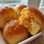 Close-up of three glazed sweet potato rolls, one torn open revealing the soft, orange interior.