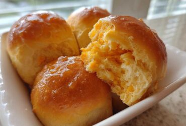 Close-up of three glazed sweet potato rolls, one torn open revealing the soft, orange interior.