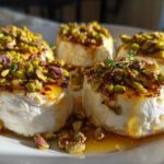 Four servings of warm goat cheese and honey bites topped with chopped pistachios and fresh thyme.
