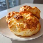 Three golden brown, fluffy cloud bread slices resting on a white plate in bright sunlight.