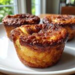 Close-up of three golden brown french toast muffins with caramelized tops sitting on a white plate.