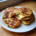 A stack of freshly cooked, golden-brown Irish potato farls resting on a white plate, showing a fluffy interior.