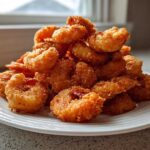 A large pile of perfectly golden brown fried shrimp stacked high on a white plate.