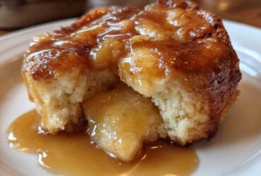 A close-up of a warm, soft apple dumpling broken open, smothered in rich caramel sauce.