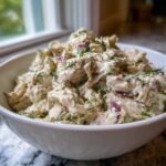 Close-up of creamy cottage cheese chicken salad with red onion and dill in a white bowl.