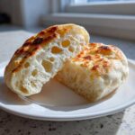 Close-up of homemade english muffins split in half, showing the airy, holey interior texture.