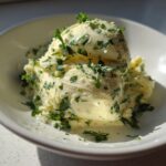 A scoop of homemade garlic butter mixed with chopped green herbs, likely parsley, served in a white bowl.