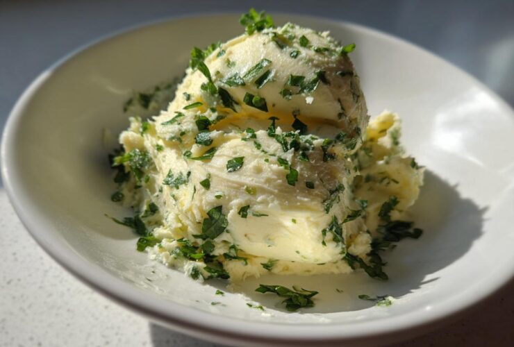 A scoop of homemade garlic butter mixed with chopped green herbs, likely parsley, served in a white bowl.
