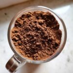 Overhead view of rich, dark brown homemade hot cocoa mix powder filling a clear glass mug.