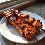 Two skewers of perfectly grilled, glazed honey garlic chicken skewers resting on a white plate.