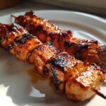 Two skewers of perfectly grilled, glazed honey garlic chicken skewers resting on a white plate.