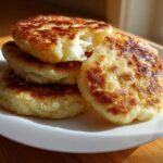 A stack of golden brown, freshly cooked Irish potato farls resting on a white plate.