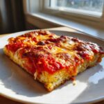 Close-up of a thick slice of pizza featuring melted cheese and rich tomato sauce on a keto pizza crust.