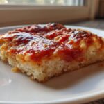 Close-up of a thick slice of keto pizza crust topped with melted cheese and bright red tomato sauce.