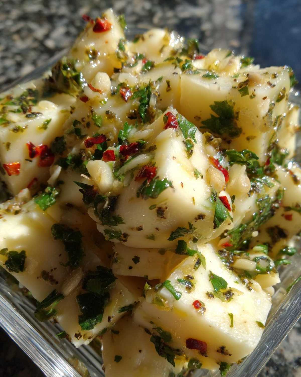 Close-up of cubed white cheese pieces coated in oil, herbs, garlic, and red pepper flakes for marinated cheese.