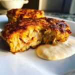 Close-up of a golden-brown Maryland crab cake cut in half, showing flaky crab meat inside, served with a dollop of creamy sauce.