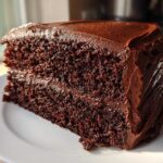 Close-up of a thick slice of moist chocolate cake recipe with dark, rich chocolate frosting.