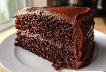 Close-up of a thick slice of moist chocolate cake recipe with dark, rich chocolate frosting.