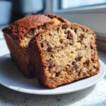 Close-up of moist date nut bread loaf with one slice cut, showing visible walnuts and raisins inside.