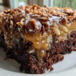 Close-up of a moist slice of german chocolate poke cake showing the dark chocolate base, gooey caramel-pecan filling, and toasted coconut topping.