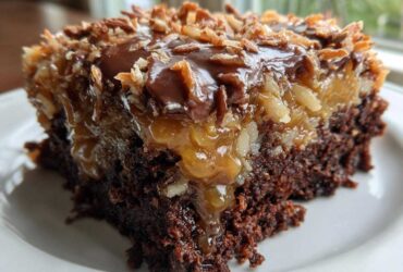 Close-up of a moist slice of german chocolate poke cake showing the dark chocolate base, gooey caramel-pecan filling, and toasted coconut topping.