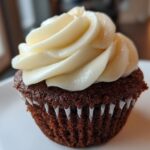 Close-up of a moist, dark gingerbread cupcake topped with a swirl of cream cheese frosting.