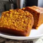 Two slices of vibrant orange, moist pumpkin bread resting on a white plate.