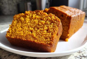 Two slices of vibrant orange, moist pumpkin bread resting on a white plate.
