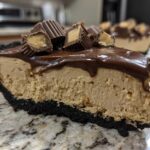 Close-up of a thick slice of no-bake peanut butter pie with a dark crust, peanut butter filling, chocolate topping, and peanut butter cups.