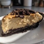 A thick slice of no bake peanut butter pie with a dark chocolate crust, topped with crumbs.