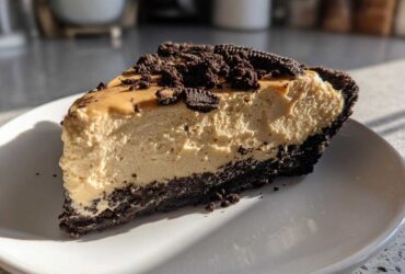 A thick slice of no bake peanut butter pie with a dark chocolate crust, topped with crumbs.