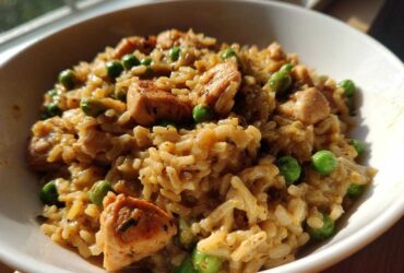 A close-up of creamy, savory one pot chicken and rice mixed with bright green peas, served in a white bowl.