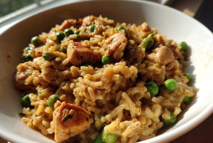 A close-up of creamy, savory one pot chicken and rice mixed with bright green peas, served in a white bowl.