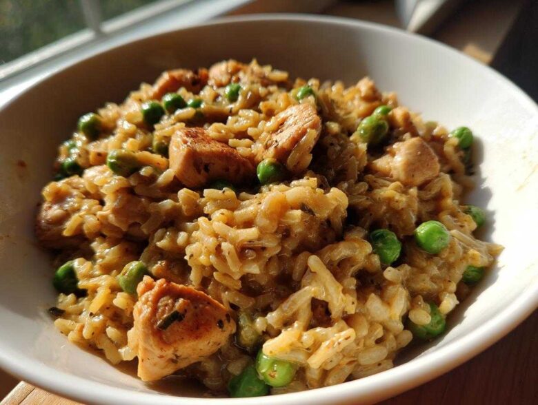 A close-up of creamy, savory one pot chicken and rice mixed with bright green peas, served in a white bowl.