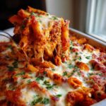A spoonful of cheesy, saucy pizza pasta being lifted from a baking dish, showing long cheese pulls.