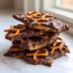 A stack of rich, dark chocolate peanut butter pretzel bark pieces showing a gooey caramel layer inside.