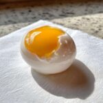 A perfectly poached eggs resting on a white napkin, showing a vibrant, runny yolk exposed at the top.