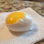 A perfectly poached eggs resting on a paper towel, showing a bright, runny yellow yolk exposed.