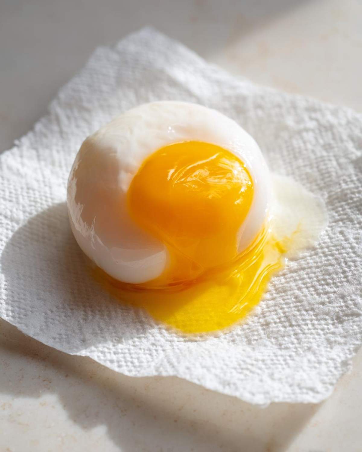 A perfectly cooked poached eggs with a bright, runny yolk spilling out onto a white paper towel.