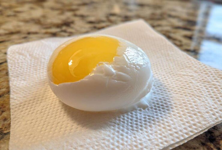 A perfectly poached eggs resting on a paper towel, showing a bright, runny yellow yolk exposed.