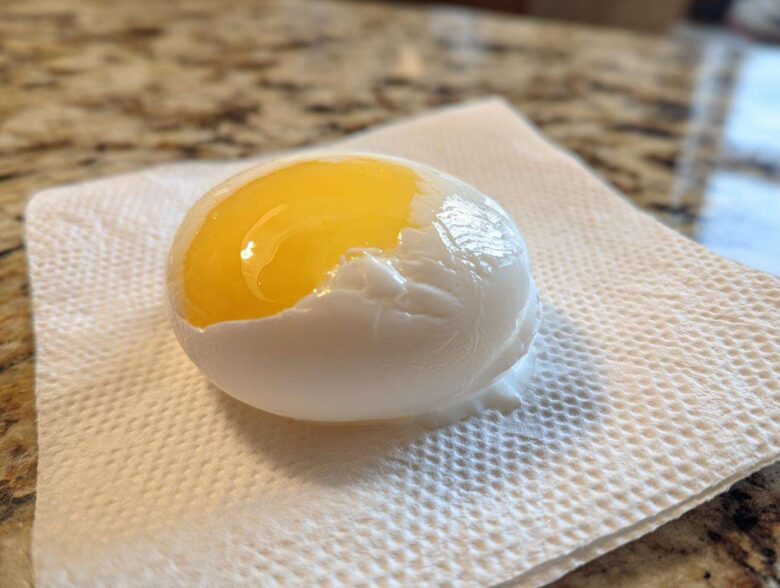 A perfectly poached eggs resting on a paper towel, showing a bright, runny yellow yolk exposed.